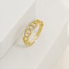 Un anillo de oro con diseño de eslabones de cadena y pequeños diamantes incrustados se muestra sobre una superficie geométrica blanca, mostrando la elegancia de las joyas en oro laminado de 18k.