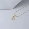 Un collar de oro con un colgante en forma de corazón adornado con pequeñas piedras reposa sobre una superficie gris, mostrando la elegancia de Joyas en Oro Laminado 18K.