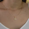 Primer plano de una persona que lleva un collar de oro con un colgante en forma de corazón, que deja ver parte del área del cuello y el pecho con un top blanco. La exquisita pieza es de la colección Joyas en Oro Laminado 18K, que aporta elegancia a cualquier outfit.