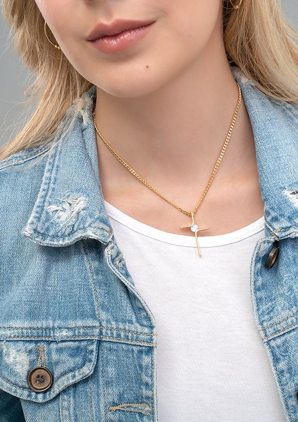 Una mujer vistiendo una chaqueta de mezclilla y una camiseta blanca, adornada con un collar de cruz de oro elaborado con exquisitas joyas en oro laminado de 18k.