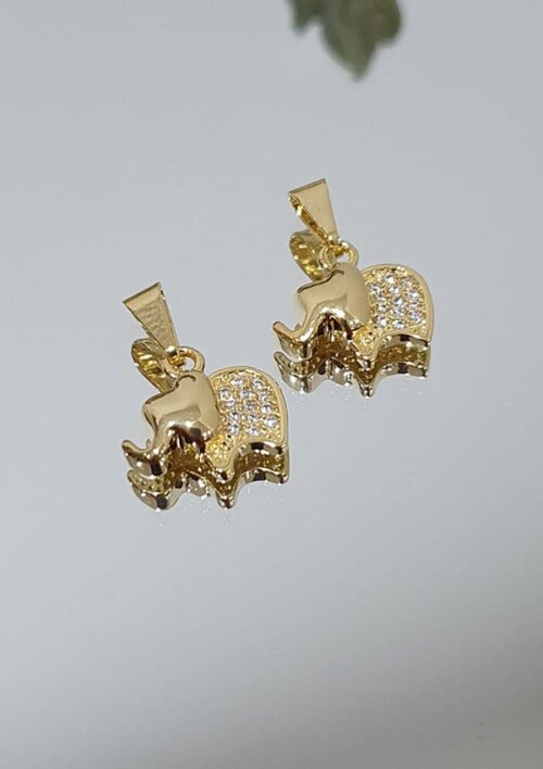 Dos colgantes en forma de elefante de oro con detalles de diamantes de imitación, colocados sobre una superficie reflectante, personifican la elegancia de las joyas en oro laminado de 18k.