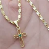 Una mano sostiene una cadena de oro con un colgante en forma de cruz que presenta una pequeña gema verde en el centro, elaborado con Joyas en Oro Laminado 18K.