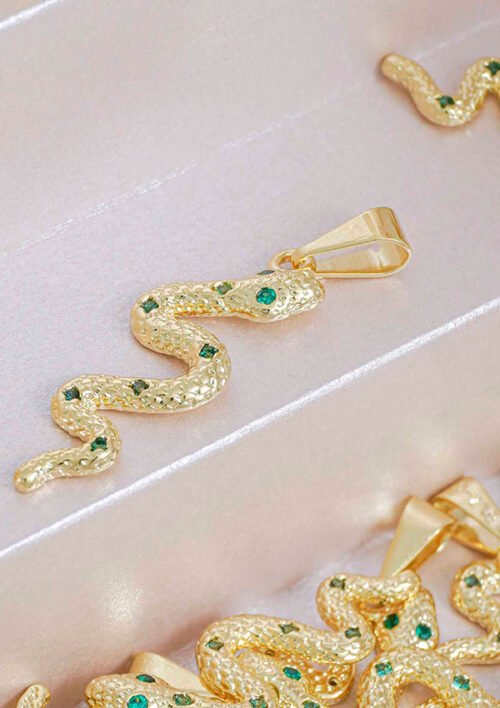 Un colgante en forma de serpiente de oro adornado con piedras preciosas verdes, exhibido en una caja de joyería, elaborado con joyas en oro laminado de 18k.