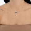 Una persona que lleva un fino collar de oro con un colgante de Dije Cruz Manto Sagrado de 1,6 Cms, un top strapless de color beige y tatuajes visibles en el cuello y los hombros adornados con joyas en oro laminado de 18k.