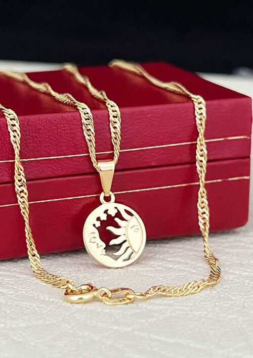 Un collar de oro con el colgante "Dije Sol y Luna", colocado sobre una caja roja, muestra la elegancia de las joyas en oro laminado 18k.