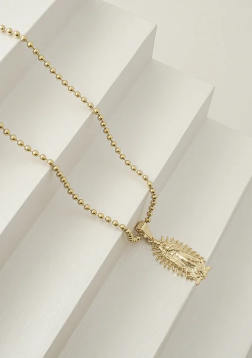 Un collar de oro con un pequeño colgante en forma de hoja de nuestra colección Joyas en Oro Laminado 18K reposa sobre un juego de escalones angulares blancos.