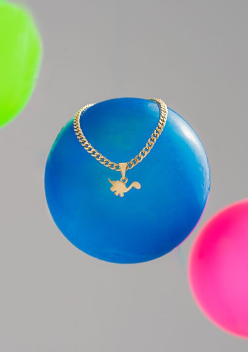 Un collar de oro con un colgante en forma de zorro se coloca sobre un globo azul, con globos verdes y rosas en el fondo, mostrando la elegancia de las joyas en oro laminado de 18k.