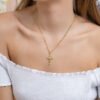 Se muestra a una persona que viste una blusa blanca con los hombros descubiertos, adornada con Joyas en Oro Laminado de 18K, que incluye un collar de oro con un colgante de cruz y pequeños aros de oro.