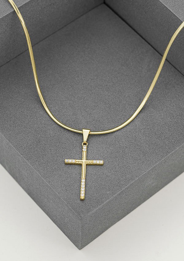 Un collar de oro con colgante de cruz adornado con pequeños diamantes, exhibido en un joyero gris, ejemplifica la elegancia de Joyas en Oro Laminado 18K.