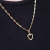 Un collar Dije Little Heart, con un colgante en forma de corazón elaborado con joyería bañada en oro de 18k, cuelga elegantemente sobre una camisa negra.