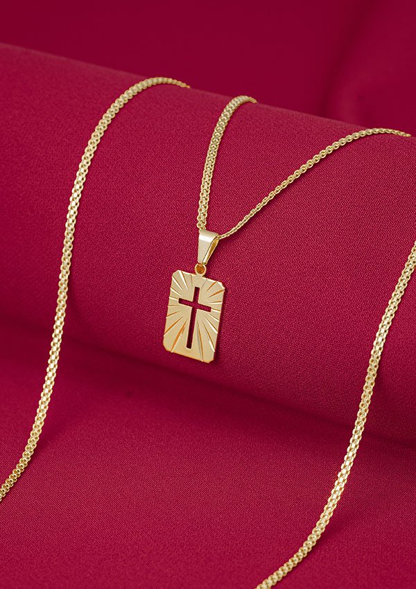 Collar de cadena de oro con dije rectangular con diseño de cruz calada, expuesto sobre tela roja. Descubre la elegancia de Joyas en Oro Laminado 18K en esta exquisita pieza.