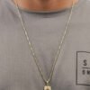 Primer plano de una persona que lleva una camisa gris y Joyas en Oro Laminado 18K, que muestra un collar de oro con un colgante rectangular que muestra una cruz. La camisa tiene un pequeño texto o logotipo parcialmente visible en el pecho.