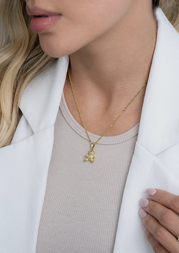 Primer plano de una persona que viste una blusa gris claro y un blazer blanco, mostrando un collar Joyas en Oro Laminado 18K con un pequeño colgante.