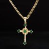 Collar de oro con colgante de cruz con piedras preciosas verdes sobre fondo negro, elaborado en Joyas en Oro Laminado 18K.