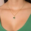 Una persona que lleva el *Dije Corazón Verde*, un collar de oro con un colgante verde en forma de corazón, vestida con un top verde, muestra la elegancia de las joyas en oro laminado de 18k.