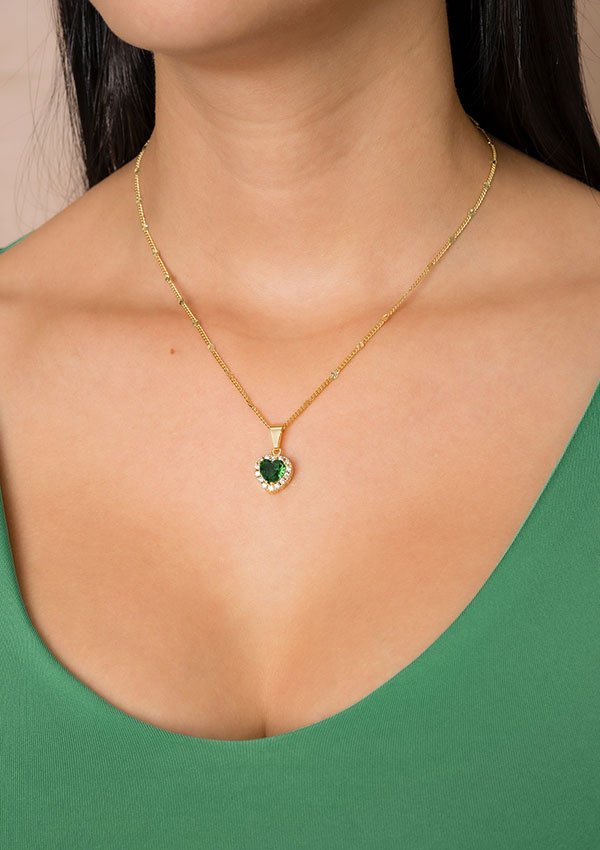 Una persona que lleva el *Dije Corazón Verde*, un collar de oro con un colgante verde en forma de corazón, vestida con un top verde, muestra la elegancia de las joyas en oro laminado de 18k.