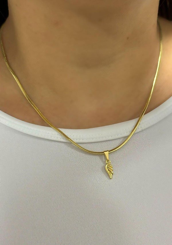 Una persona que lleva un collar de oro con un pequeño colgante de pluma de oro sobre una camisa blanca, mostrando la elegancia de las joyas de Dije Ala en oro laminado de 18k.