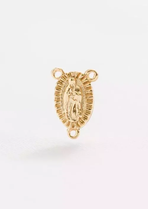 El Herraje tipo Crucero Virgen de Guadalupe es una pequeña medalla religiosa de color dorado con tres agujeros, presentando una figura central, lo que la convierte en un conector ideal para crear Joyas en Oro Laminado 18K.