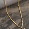 Un collar colgante de oro con un dije rectangular grabado, exhibido sobre una superficie de piedra junto a una tela enrollada. Esta impresionante pieza es parte de nuestra exclusiva colección de joyas en oro laminado de 18k y se llama "Dije El Señor es mi Pastor".