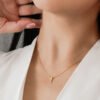 Primer plano de una persona que lleva un collar bañado en oro de 18k con un pequeño colgante, vestida con una prenda blanca.