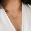 Una mujer vestida con un top blanco exhibe un collar de oro que tiene un pequeño colgante con la letra "p", mostrando la elegancia de las joyas en oro laminado de 18k.