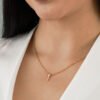 Se muestra a una persona vistiendo un top blanco de hombros hacia arriba, luciendo un collar de oro con un pequeño colgante en forma de cruz, elaborado con joyas en oro laminado de 18k.