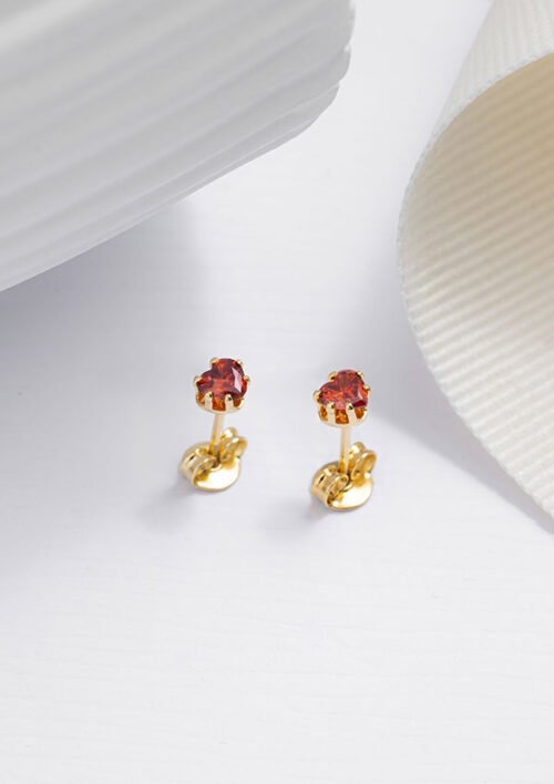 Un par de aretes de oro con detalles de piedras rojas, elaborados con joyas en oro laminado de 18k, colocadas sobre una superficie blanca.