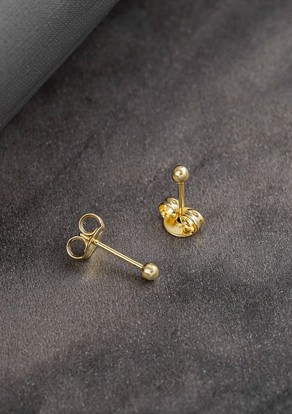 Dos aretes de oro, uno colocado boca arriba mostrando el poste y el cierre, y el otro en posición vertical mostrando el frente. Estos exquisitos Aretes Balin #2 elaborados en Oro laminado de 18K son perfectos para cualquier ocasión.