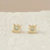 Par de aretes en forma de estrella de oro con piedras preciosas transparentes en el centro, mostrando la elegancia de Joyas en Oro Laminado 18K, colocados sobre un fondo de tela blanca texturizada.