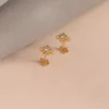 Par de aretes de oro con diseño de estrella, sobre un suave fondo de tela en tonos beige y gris. Estas exquisitas piezas de Joyas en Oro Laminado 18K destilan elegancia y sofisticación.