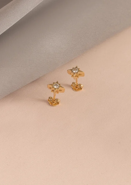 Par de aretes de oro con diseño de estrella, sobre un suave fondo de tela en tonos beige y gris. Estas exquisitas piezas de Joyas en Oro Laminado 18K destilan elegancia y sofisticación.