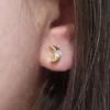 Primer plano de una oreja adornada con un pendiente de media luna de oro, engastado con un pequeño diamante, de la colección Joyas en Oro Laminado 18K.