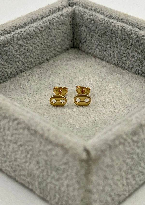 Un par de aretes de oro con un diseño minimalista, elaborados con Joyas en Oro Laminado de 18K, colocados dentro de una caja de joyería cuadrada forrada de tela gris.