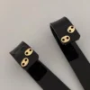 Dos pulseras negras con cierres metálicos de color dorado, que recuerdan a Joyas en Oro Laminado 18K, descansan sobre una superficie gris.