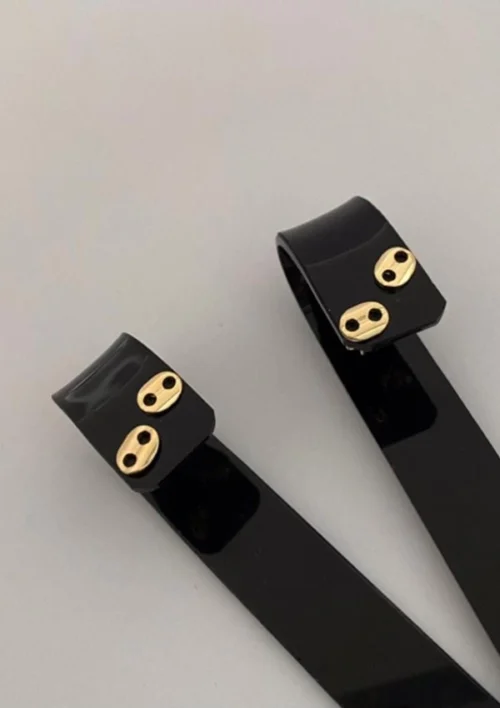 Dos pulseras negras con cierres metálicos de color dorado, que recuerdan a Joyas en Oro Laminado 18K, descansan sobre una superficie gris.