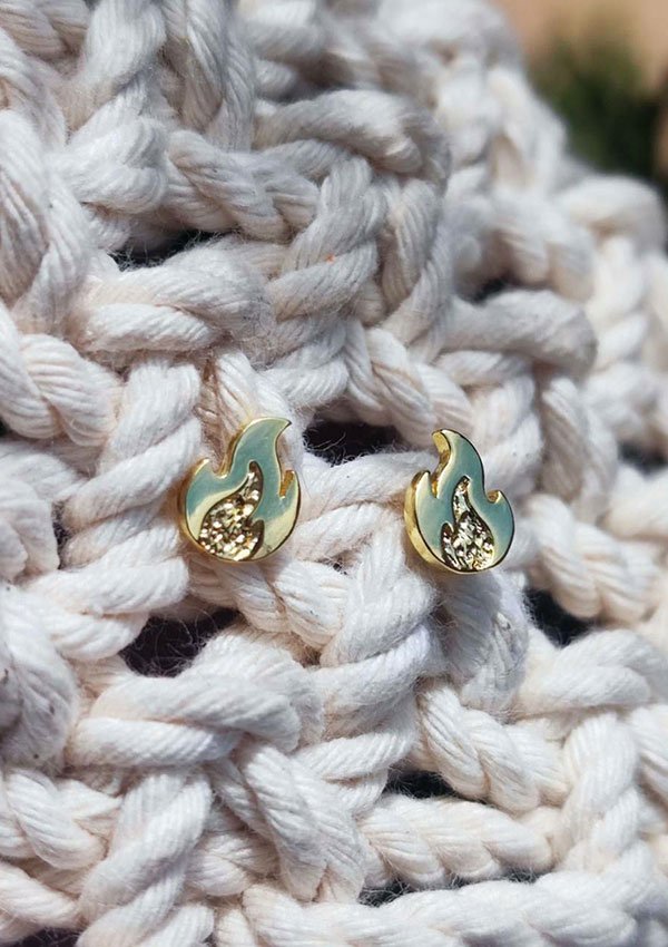 Aretes en forma de llama de oro y verde con pequeños detalles de diamantes, elaborados por expertos como Joyas en Oro Laminado 18K, exhibidos sobre una tela de punto blanca.