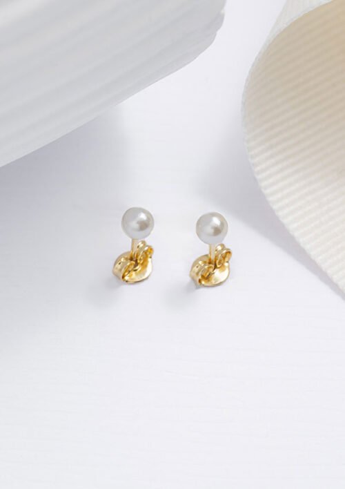 Un par de Aretes Perla de 4 mm, con aretes de oro con tapas de perlas blancas, se exhiben sobre una superficie blanca junto a una tela texturizada blanca. Estas exquisitas joyas están hechas de oro laminado de 18 quilates, añadiendo un toque de elegancia atemporal a cualquier conjunto.