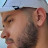 Primer plano de una persona con barba y gorra blanca, mirando hacia un lado. La persona tiene un pequeño pendiente en forma de rayo en la oreja, que brilla como Joyas en Oro Laminado 18K.