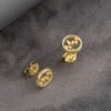 Gemelos Aretes Wave de oro laminado de 18K con diseños circulares de líneas onduladas, colocados sobre una superficie de textura oscura junto a un tejido gris.