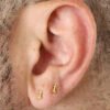 Primer plano de una oreja adornada con dos aretes de oro en forma de flecha en el lóbulo. La oreja se muestra sobre un fondo muy recortado, lo que muestra la elegancia de Joyas en Oro Laminado de 18K.