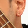 Primer plano de la oreja de una persona que lleva un pendiente de nota musical de oro, elaborado con Joyas en Oro Laminado de 18K, con el borde del mástil de una guitarra visible en primer plano.