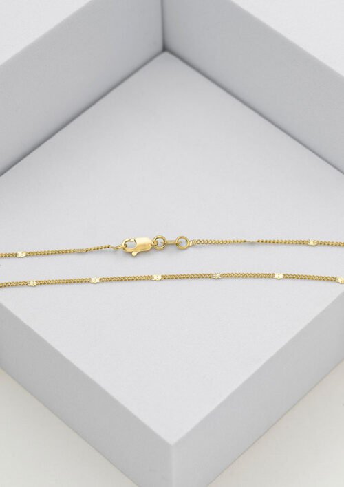 Un delicado collar de cadena bañado en oro de 18k con pequeños detalles redondos se presenta cuidadosamente en una caja gris. La Cadena Cubana Con Destellos 45Cm, parte de nuestra exquisita colección de joyas en oro laminado, se asegura con un broche de pinza de langosta y un anillo circular.