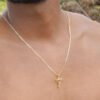 Primer plano de una persona sin camisa que lleva la Cadena Cubana Plana Diamantada de 65 cm con un colgante de crucifijo elaborado con joyas en oro laminado de 18 k sobre un fondo natural borroso.