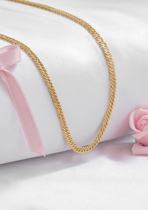 Collar de cadena de oro expuesto sobre tela blanca con lazo rosa y rosa rosa de fondo, mostrando la elegancia de Cadena Continua 3 mm 45 cms en baño de oro de 18k.