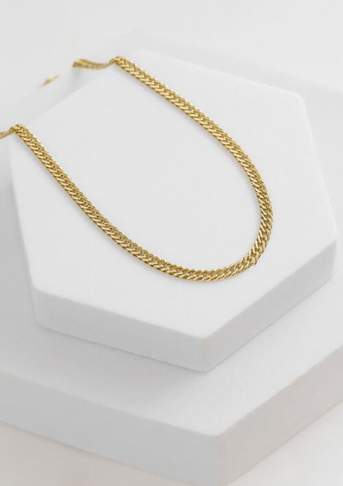 Un collar de cadena de oro se exhibe sobre un soporte geométrico blanco, mostrando la elegancia de la Cadena Continua 3 Mm 65 Cms.