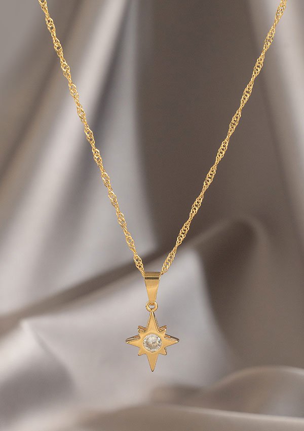 Un collar de oro, la Cadena Singapur 1.5 mm 45 Cms, con un colgante en forma de estrella que presenta una piedra preciosa central, se muestra sobre un fondo suavemente difuminado, mostrando la elegancia de las joyas en oro laminado de 18k.