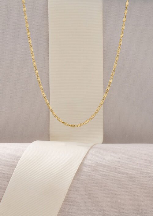 Un delicado collar, específicamente la Cadena Caracol Gruesa 45 Cms elaborado con joyas en oro laminado de 18k, cuelga sobre un fondo beige con una cinta blanca vertical.