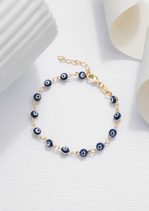 Pulsera Ojo Turco 16 Cms + Extensor que presenta una pulsera de cadena de oro adornada con cuentas azules y blancas en forma de ojos, elegantemente dispuestas sobre una superficie blanca plana con elementos decorativos en el fondo. Esta impresionante pieza es parte de nuestra colección Joyas en oro laminado de 18k, que ofrece elegancia y belleza atemporal.