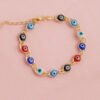 La Pulsera Ojo Turco Multicolor 16 Cms + Extensor es una pulsera de cadena de oro adornada con dijes circulares alternados en rojo, azul y negro, cada uno con un diseño de ojo. Se presenta hermosamente sobre una superficie texturizada rosa y está elaborada con joyas en oro laminado de 18k para una mayor elegancia y durabilidad.