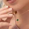 Una persona de piel clara sostiene un collar de oro con una gema verde, mientras lleva una blusa de color claro. Esta impresionante pieza forma parte de la colección Joyas en Oro Laminado 18K.